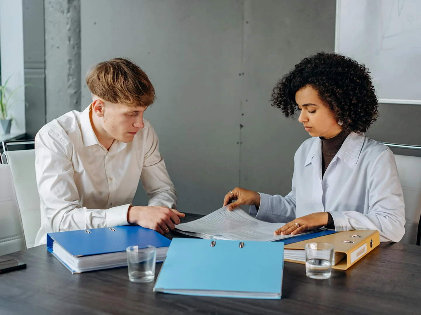 A patient and a healthcare professional sit across a desk reviewing paperwork together